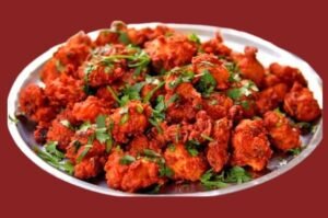 Spicy fried Chicken 65 garnished with curry leaves, green chilies, and lemon wedges
