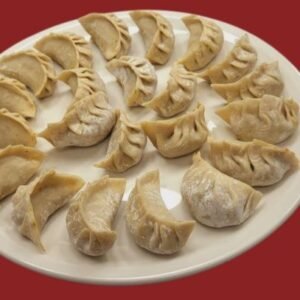 A plate of steamed Veg Momos served with spicy red chili chutney and garnished with fresh herbs.